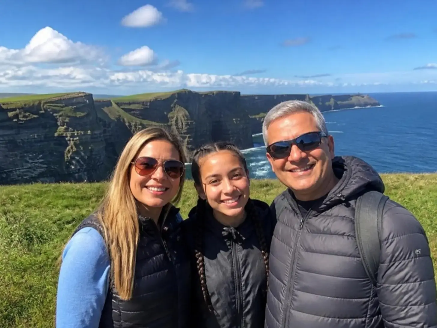 Família sorrindo nas Falésias de Moher, na Irlanda, com o mar ao fundo